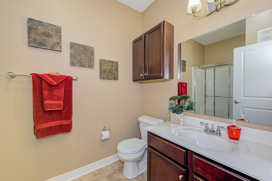 Add a splash of color to brighten up your bathroom. Bathroom at The Waverly Apartments. Beige walls with dark brown cabinets plus red decor inside a bathroom at The Waverly Apartments.