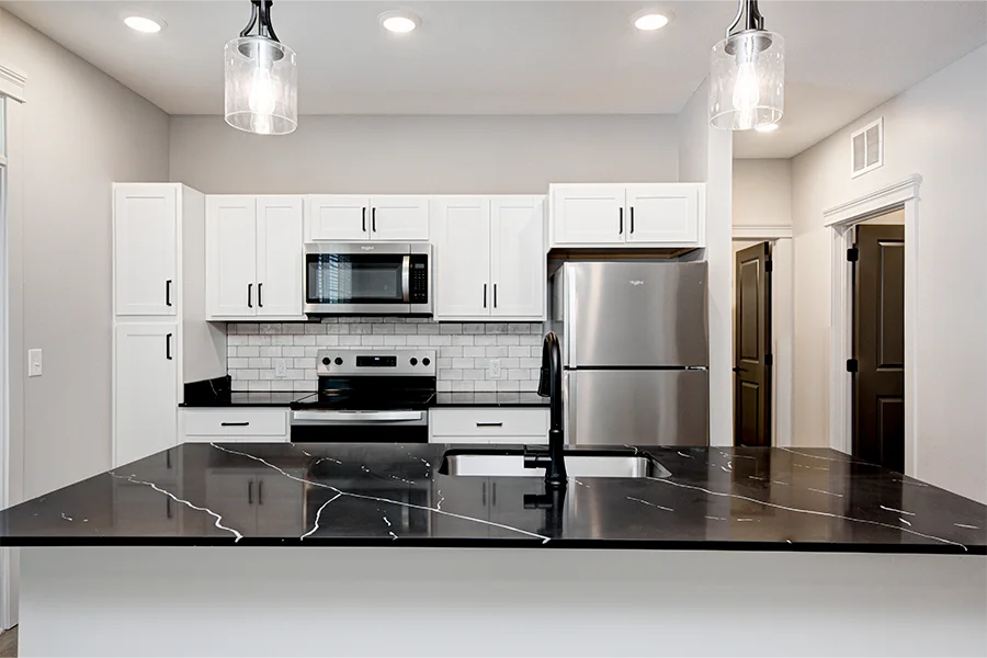 High-end materials and finishes like these quartz kitchen counters at Hyde Park Apartments Apartment kitchen with black quartz countertop, white subway tile blacksplash, and stainless steel appliances