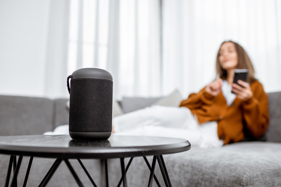 Use a smart speaker to conveniently control other devices in your Noblesville apartment. Woman sitting on a sofa beside a smart speaker on a coffee table
